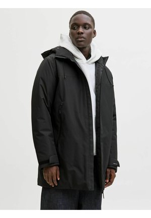 Juodas vandeniui atsparus parkas su kapišonu, užtrauktukais šoninėse kišenėse ir reguliuojamais rankogaliais. Viduje yra šviesiai pilkas džemperis.