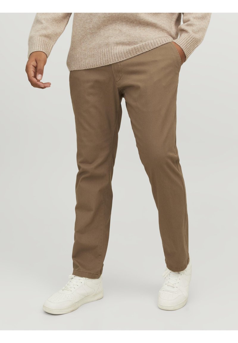 Pantaloni chinos marroni in misto cotone con vestibilità dritta, dotati di tasche laterali e una texture liscia. Abbinati a scarpe da ginnastica bianche.