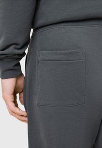 Szare bawełniane dresy z widoczną naszywaną kieszenią z tyłu, o gładkiej fakturze i elastycznym pasie.