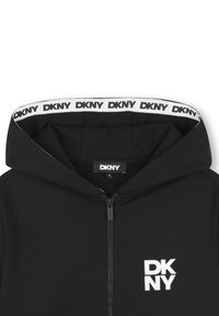 Sweat à capuche zippé noir avec un logo DKNY blanc sur la poitrine et une bordure côtelée à marque déposée le long du bord intérieur de la capuche.