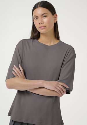 Grå kortærmet T-shirt med rund halsudskæring og afslappet pasform, der har en glat stof og et minimalistisk design. Modellen poser med korslagte arme.