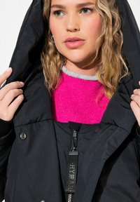 Chaqueta negra con capucha y suéter interior en tonos rosa y gris. Cuenta con cierre de cremallera, botones a presión y tela texturizada.