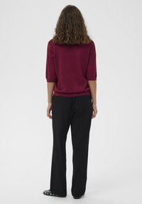 Burgundská vlnená mikina s tromi štvrtinovými rukávmi v kombinácii s čiernymi širokými nohavicami a detailne spracovanými čiernymi slip-on topánkami.