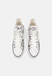 Tenisky s vysokým svrškem s černobílým kresleným vzorem na plátně, s bílými tkaničkami, gumovou podrážkou a černým lemováním.