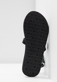 Semelle de sandale noire avec le logo de la marque Roxy embossé dans un motif répétitif ; présente une forme profilée et une texture douce.