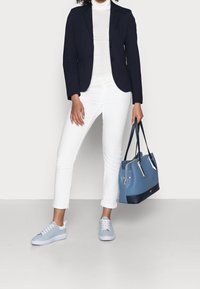 Borsa in pelle blu con dettagli blu navy, abbinata a jeans slim-fit bianchi e sneaker azzurri chiari, con punta arrotondata e lacci.