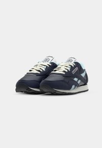Baskets de sport bleu marine avec des détails bleu clair, présentant un dessus en synthétique lisse, des lacets blancs et une semelle en caoutchouc texturée.