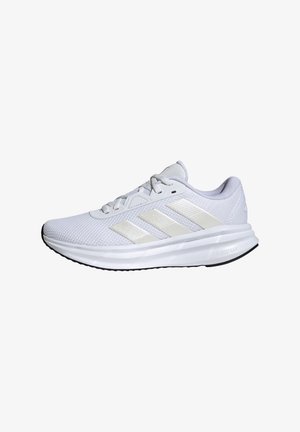 Chaussure de course blanche Adidas avec trois bandes beige, dessus en mesh, design à lacets et semelle épaisse coussinée appelée « Cloudfoam ».