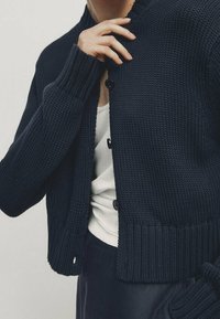 Marineblauwe gebreide cardigan met een ronde halslijn, knoopsluitingen, geribbelde boorden en zoom. Textuurstof en een cropped ontwerp met een ontspannen pasvorm.