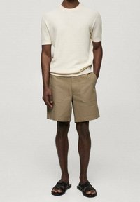 Kremowy sweter o prążkowanej strukturze z krótkim rękawem, w połączeniu z beżowymi szortami cargo z przednimi kieszeniami i prostym krojem, uzupełniony czarnymi sandałami.