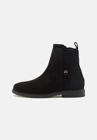 Stivali Chelsea in pelle scamosciata nera con pannelli elastici, suole piane e un bordo per indossarli facilmente. Caratterizzati da un design minimalista e dettagli testurizzati.