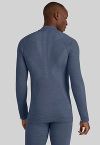 Długi rękaw sportowej koszulki w ciemnoniebieskim kolorze, z teksturowanymi wzorami i dopasowanym krojem, z okrągłym dekoltem i otworami na kciuki w mankietach.