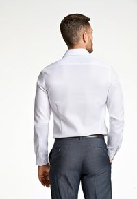 Witte langemouwen shirt met een klassieke kraag, voorzien van knoopmanchetten. Draagt met donkere, op maat gemaakte pantalon, die een soepele textuur en pasvorm toont.
