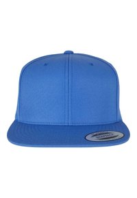 Kék snapback sapka strukturált anyagból, lapos karimával. Elöl egy kerek címke található, amely a márkát mutatja be.