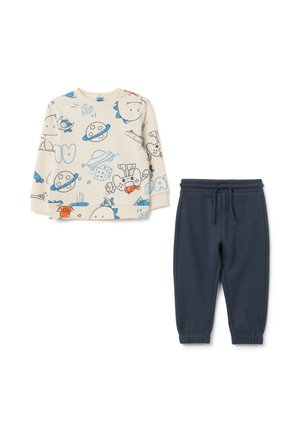 Helle beige Longsleeve-Bluse mit Cartoon-Drucken, kombiniert mit dunkelblauen, schmal geschnittenen Jogginghosen mit elastischem Bund.