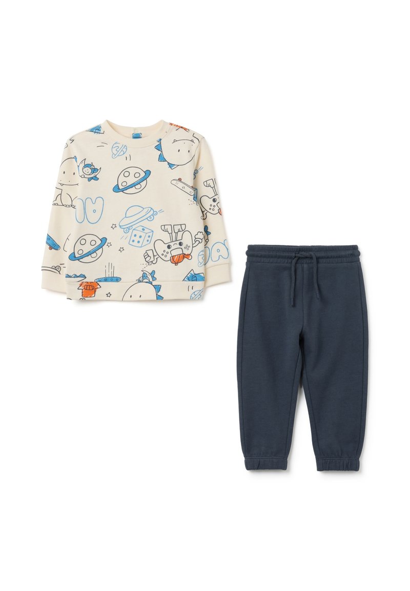 Haut à manches longues beige clair avec des imprimés de dessins animés, associé à un pantalon de jogging tapered bleu foncé avec une taille élastique.