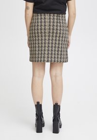 Mini-jupe à motif pied-de-poule en beige et noir, en tissu texturé, avec une coupe ajustée et une fermeture éclair à l'arrière. Assortie à des bottines à talons block.