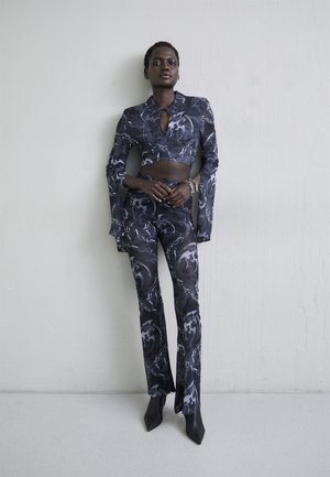 Melna un pelēka rakstota divdaļīga apģērba komplekts, kas ietver īsu topu ar apkakli un atslēgvietu, plati piedurknes un pieguļošas bikses.