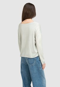 Hellgrauer Langarmpullover mit weitem Ausschnitt, weicher Textur und überschnittenen Schultern, kombiniert mit lockeren blauen Jeans.