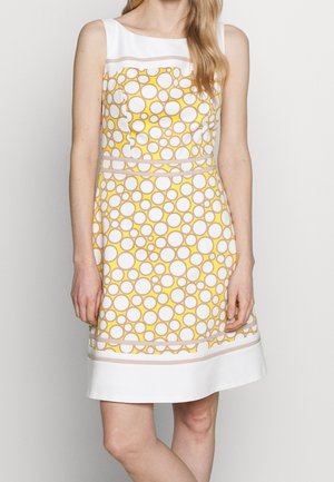 Robe blanche sans manches avec un motif circulaire jaune et beige, taille cintrée et détails de bordure horizontale transparente au-dessus de l'ourlet et de la poitrine.