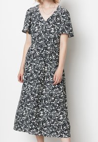 Svartvitt blommönstrat klänning med korta ärmar, v-ringning, åtsittande midja och en fladdrig klänning med medellängd. Mjuk tygtextur.