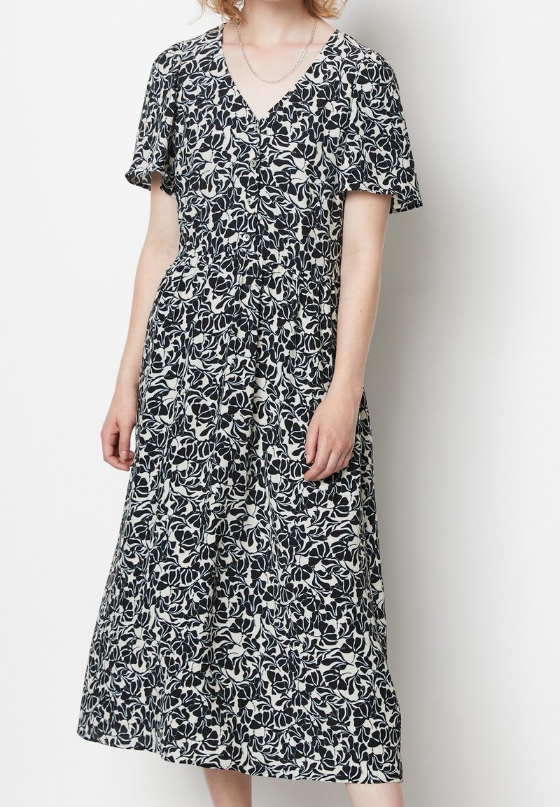 Svartvitt blommönstrat klänning med korta ärmar, v-ringning, åtsittande midja och en fladdrig klänning med medellängd. Mjuk tygtextur.