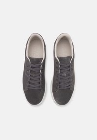 Zapatillas de ante gris con punta redonda, suela blanca plana y cordones a juego. El interior presenta un acolchado gris claro con una marca en relieve.