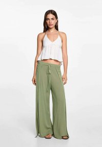 Biely halter top s rozšíreným dizajnom, doplnený voľnými, svetlozelenými nohavicami s širokými nohavicami a viazaním v páse. Hladká textúra, pohodlný štýl.
