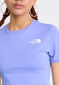 Vaaleanlila puuvillapaita, jossa on lyhyet hihat ja vasemmassa rinnassa valkoinen brodeerattu "The North Face" -logo.