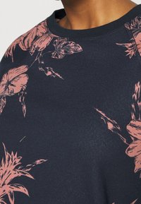 Marineblå sweatshirt med pink blomsterprint, rund halsudskæring og tekstureret stof, der fremhæver indviklede blomsterdetaljer på skulderen.
