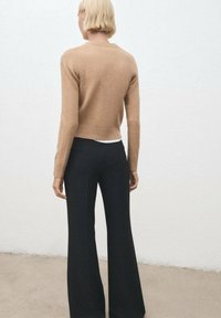 Suéter corto marrón con un diseño ajustado, combinado con pantalones de pierna ancha de canalé oscuros. Textura suave, líneas simples y paleta de colores neutros.