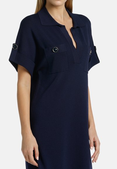 Abito polo blu navy con maniche corte, dotato di due tasche frontali con dettagli a bottone e un collo con pattina per una vestibilità rilassata.