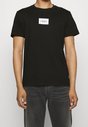 Black cotton t-shirt with short sleeves, round neckline, and a white rectangular logo patch reading "CALVIN KLEIN JEANS" on the chest.