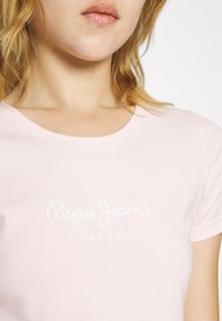 Světle růžové bavlněné tričko s kulatým výstřihem a bílým potiskem "Pepe Jeans LONDON" na přední straně. Hladký povrch a přiléhavý střih.