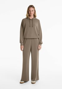 Beige hoodie with drawstrings, paired with matching wide-leg trousers. Soft texture and relaxed fit. White and tan shoes complete the ensemble.