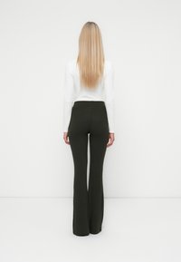 Geribbelde, donkergroene wijde broek met hoge taille, gecombineerd met een witte blouse met lange mouwen, bekeken vanuit de achterkant. Gladde textuur, rekbaar materiaal.