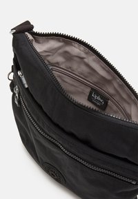 Borsa a tracolla nera in sintetico con apertura con zip. I dettagli includono una piccola tasca interna, una patch con logo e un tessuto testurizzato.