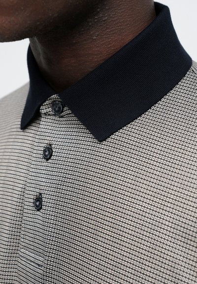 Trumpas rankovėmis polo marškinėliai su geometriniu raštu tamsių ir šviesių spalvų, išsiskiriantys tamsiai mėlynu apykakle ir trimis juodais mygtukais.