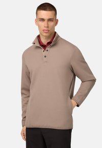 Maglione marrone texturizzato con colletto alto, dotato di una patta con bottoni e maniche lunghe, indossato sopra una camicia bordeaux.