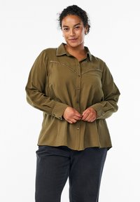 Olive green button-up shirt with a collar, long sleeves, and silver embellishments along the yoke, featuring a textured fabric and relaxed fit.