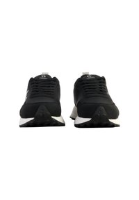 Scarpe sportive nere con tomaia in tessuto liscio, dettagli testurizzati e suola intermedia bianca. Presentano lacci tradizionali e un colletto imbottito.