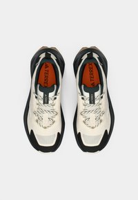 Ζευγάρι λευκά και μαύρα παπούτσια Adidas Terrex για τρέξιμο σε μονοπάτι με κορδόνια με σχέδιο και κόκκινες εσωτερικές σόλες, σε λευκό φόντο, με θέα από πάνω.