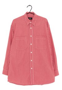 Camicia a maniche lunghe a quadretti rossi e bianchi con colletto e due taschini sul petto appesa a un gancio nero.