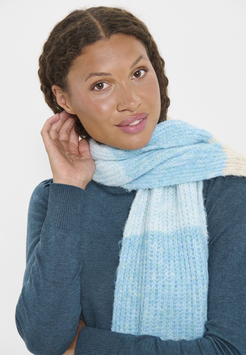 Világoskék és krémszínű csíkos sál, puha, texturált anyagból készült, változatos árnyalatokkal és kötött mintával.