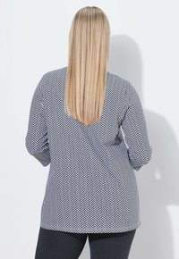 Zwart-wit herringbone-patroon top met lange mouwen, gecombineerd met zwarte leggings. De stof lijkt glad en lichtjes textuur te hebben.