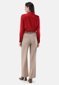Rote Seidenbluse mit Kragen, kombiniert mit beigen hoch taillierten Hosen. Detaillierte Nähte und ein Gürtel betonen die Taille.