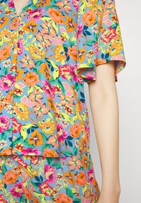 Top de manga curta floral com um fundo azul e flores multicoloridas em tons de rosa, laranja e amarelo; tecido texturizado com um corte descontraído.