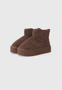 Brązowe zamszowe botki za kostkę z okrągłym noskiem, teksturowaną elastyczną boczną wstawką oraz grubą gumową podeszwą. Minimalistyczny design o niskim profilu.