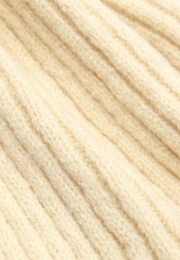 Beige gebreide stof met een geribbelde textuur, voorzien van zachte, pluizige vezels en subtiele variaties in diepte en lichtreflectie.