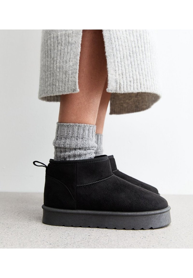 Czarne zamszowe botki za kostkę z grubą szarym gumowym podeszwa, z uchwytem do łatwego zakładania. Połączone z jasnoszarymi wełnianymi skarpetkami.